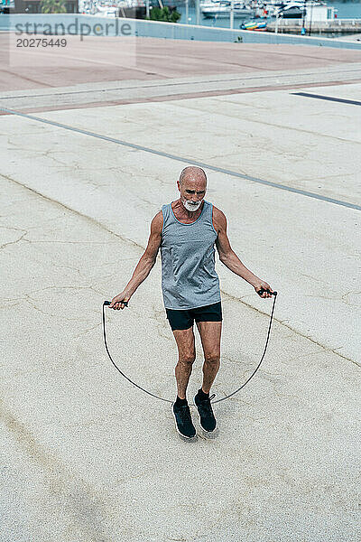 Aktiver älterer Mann trainiert mit Springseil auf Fußweg