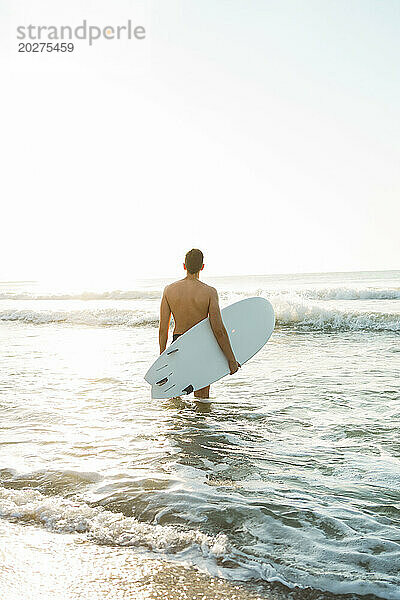 Junger Mann hält Surfbrett am Strand