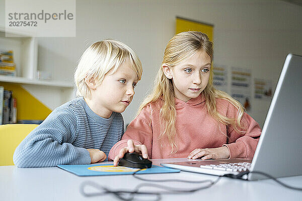 Mädchen und Jungen teilen sich einen Laptop  um im Schulklassenzimmer Computerprogrammierung zu lernen