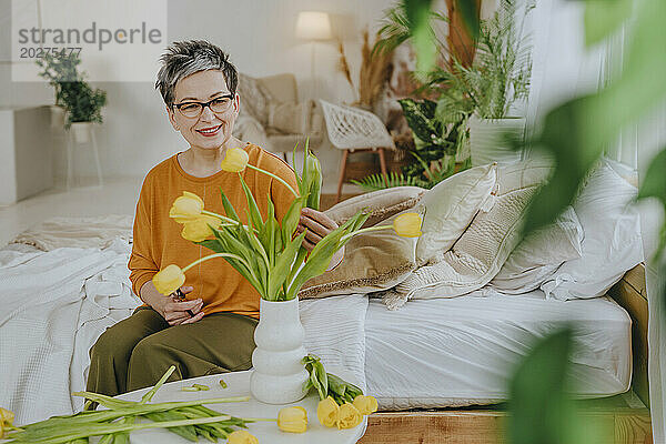 Lächelnde Frau arrangiert zu Hause Tulpen in einer Vase