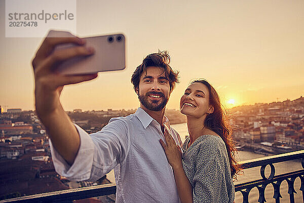 Lächelndes Paar macht ein Selfie mit dem Smartphone vor dem Fluss Douro bei Sonnenuntergang  Porto  Portugal