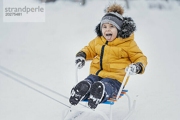 Fröhlicher Junge in warmer Kleidung genießt im Winter eine Schlittenfahrt im Schnee