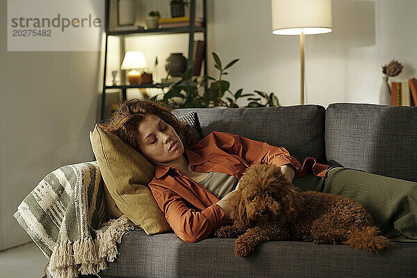 Müde schwangere Frau ruht sich zu Hause mit Hund auf dem Sofa aus
