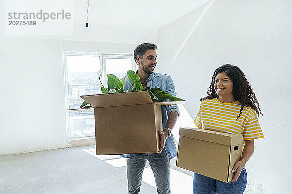 Smiling couple carrying cardboard boxes at new home