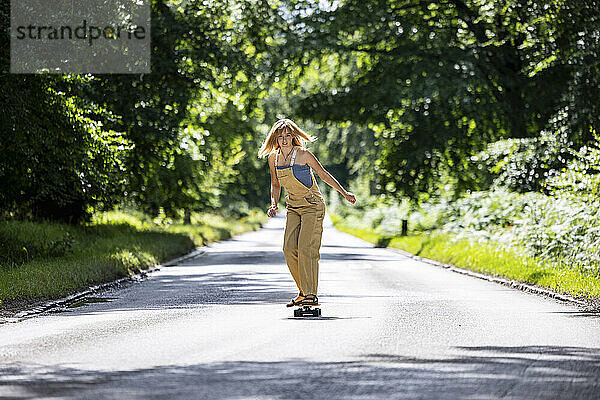 Junge Frau fährt Skateboard auf der Straße im Wald