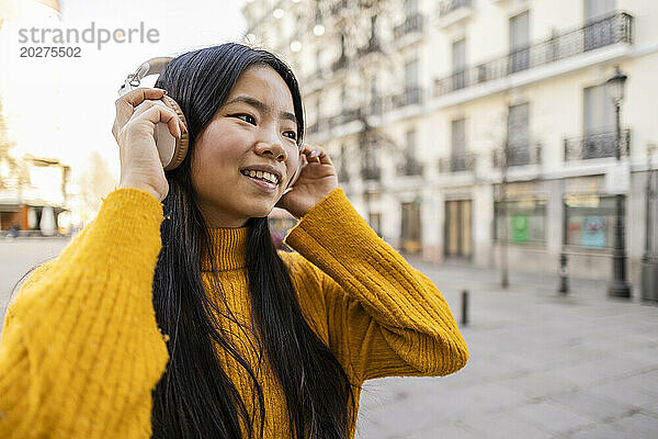Glückliche junge Frau mit kabellosen Kopfhörern in der Nähe eines Gebäudes