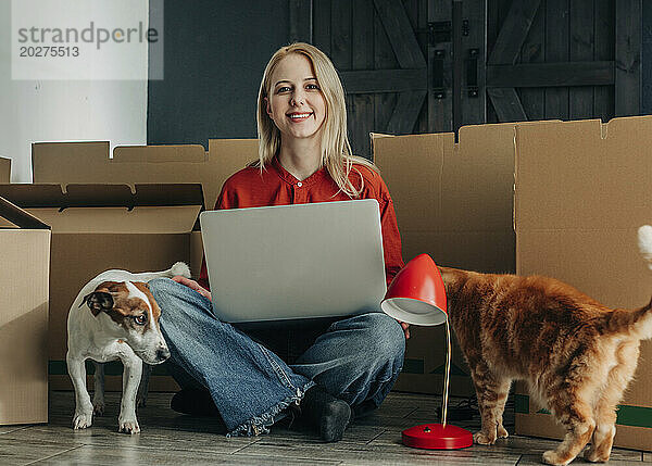 Glückliche Frau sitzt mit Haustieren und Laptop zu Hause