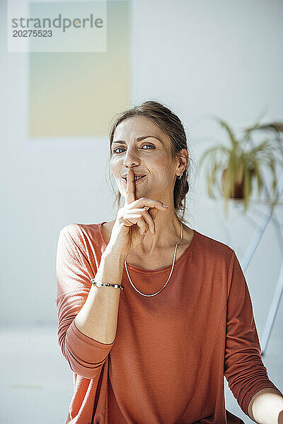 Smiling woman with finger on lips at home