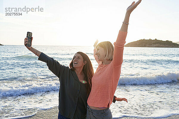 Sorglose Freunde mit ausgestreckten Armen machen Selfie am Strand