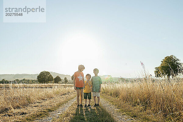 Kinder stehen bei Sonnenuntergang auf unbefestigter Straße im Feld