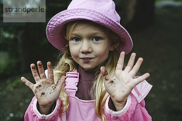 Mädchen in rosa Regenmantel und Hut zeigt schmutzige Hände