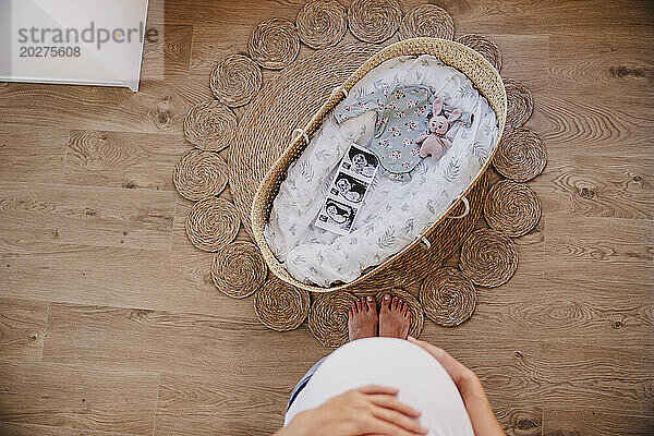 Schwangere Frau steht zu Hause neben einem Korb auf einem Teppich