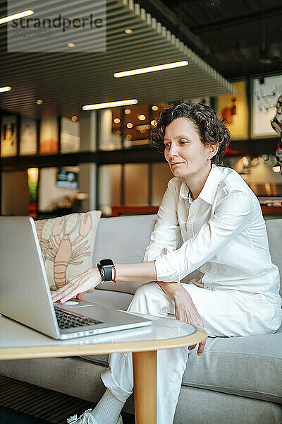 Selbstbewusste Geschäftsfrau sitzt mit Laptop auf dem Sofa in der Hotellobby
