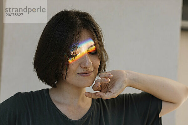 Woman with rainbow colored light reflection on face