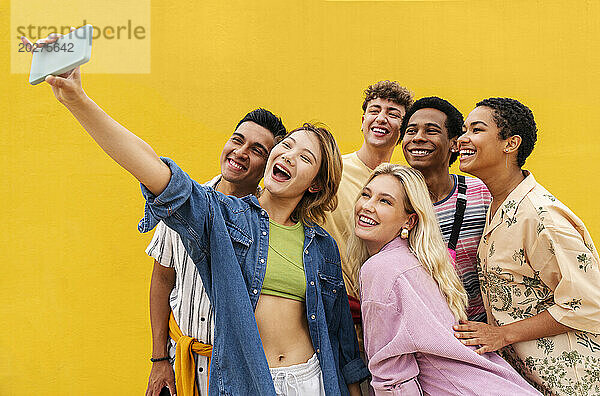 Lachende multiethnische Freunde machen Smartphone-Selfies vor gelber Wand