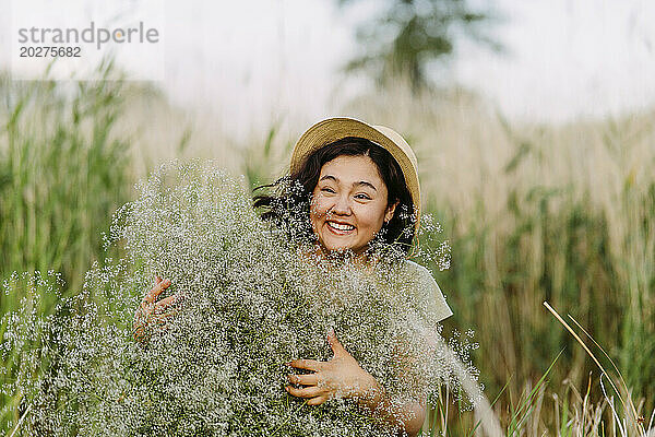 Fröhliche Frau mit Hut und einem Strauß Schleierkrautblüten im Feld
