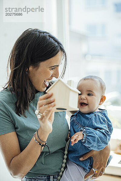 Fröhliche Mutter zeigt ihrer kleinen Tochter ein hölzernes Modellhaus