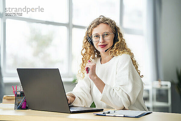 Lächelnde Verkäuferin mit Headset neben Laptop im Büro