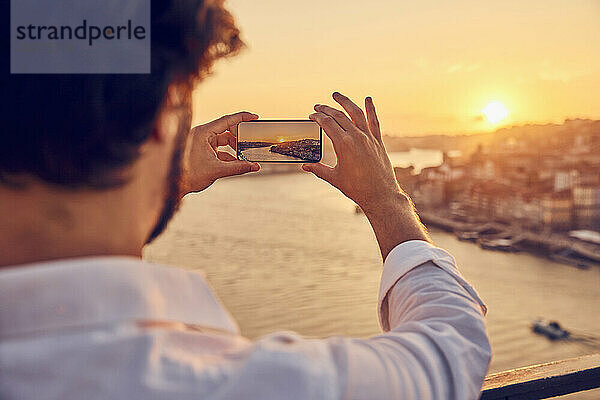 Mann fotografiert die Stadt Porto mit dem Smartphone bei Sonnenuntergang in Portugal