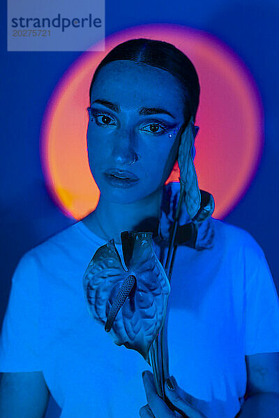 Frau hält Anthuriumblume vor Gesicht in neonblauer Beleuchtung
