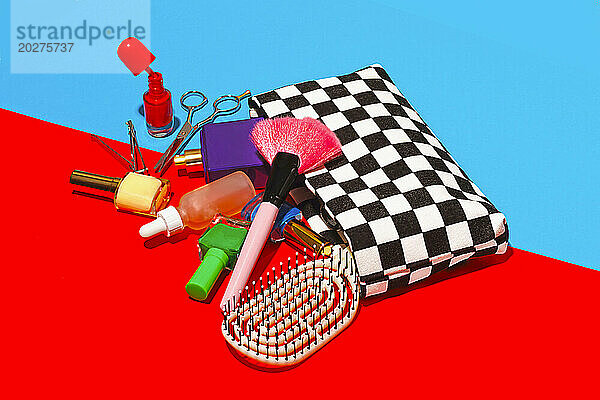 Studio shot of various cosmetics falling out of checked purse