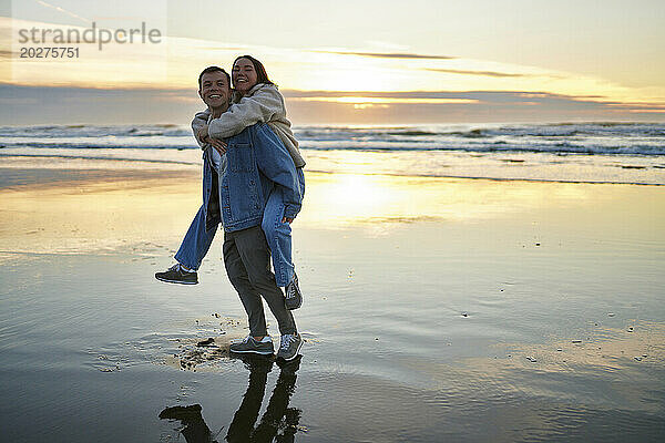 Lächelnder Mann trägt Freundin huckepack am Meeresstrand