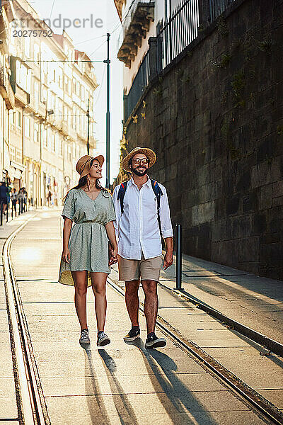 Glückliches junges Paar hält Händchen und läuft auf Straßenbahnschienen in der Stadt