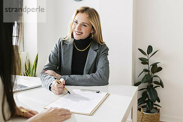 Happy businesswoman explaining contract to colleague at desk