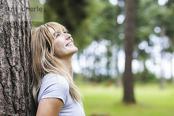 Lächelnde junge Frau  die sich an einen Baumstamm lehnt