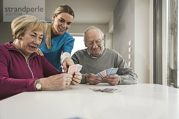 Glückliches älteres Paar  das mit der häuslichen Pflegekraft am Tisch Karten spielt