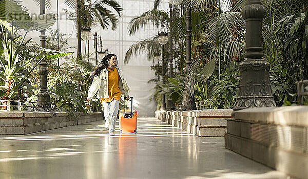 Glückliche Frau  die mit Koffer in der Nähe von Pflanzen läuft