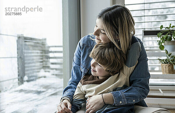 Lächelnde Mutter sitzt mit Sohn zu Hause am Fenster