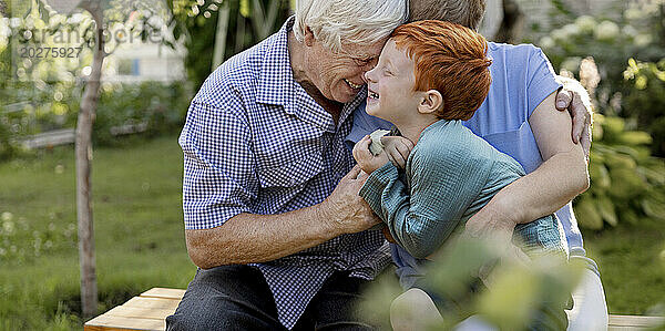Fröhlicher Junge amüsiert sich mit Großeltern  die auf einer Bank im Garten sitzen