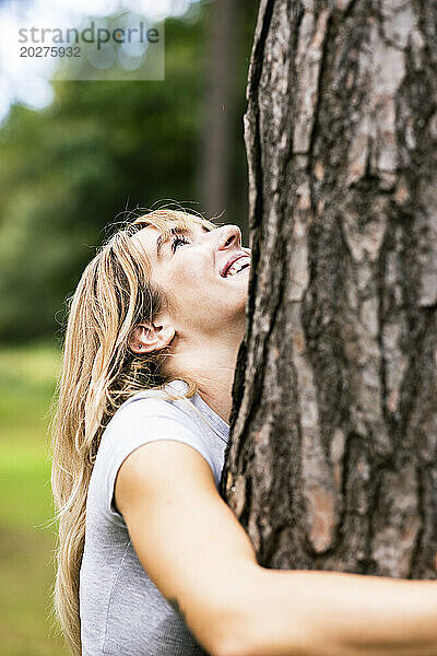 Glückliche schöne Frau  die Baum umarmt