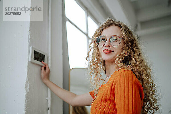 Lächelnde Frau in der Nähe des Thermostats an der Wand zu Hause
