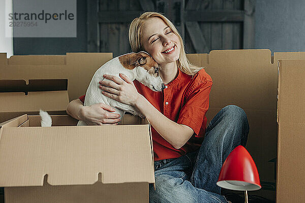 Glückliche Frau umarmt Hund in der Nähe von Kartons zu Hause
