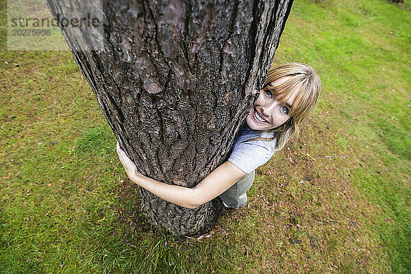 Lächelnde schöne Frau umarmt Baum