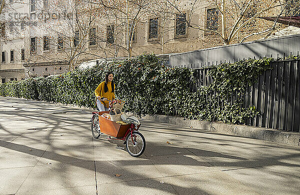 Junge Frau fährt Lastenfahrrad in der Nähe von Pflanzen auf Fußweg