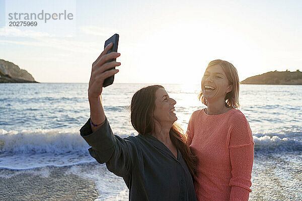 Cheerful friends taking selfie together on shore at beach