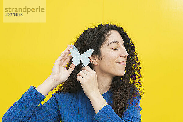 Lächelnde Frau mit Schmetterling im Haar vor gelbem Hintergrund