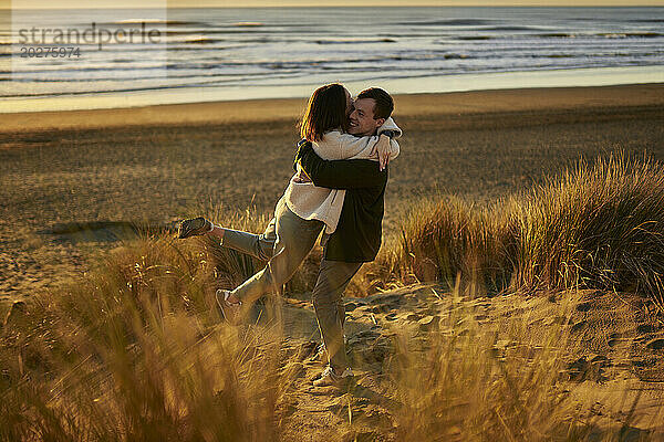 Glücklicher junger Mann umarmt und dreht Frau am Strand