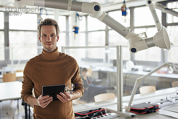 Lächelnder Ingenieur hält Tablet-PC in der Hand und steht in der Nähe des Absaugarms in der Werkstatt