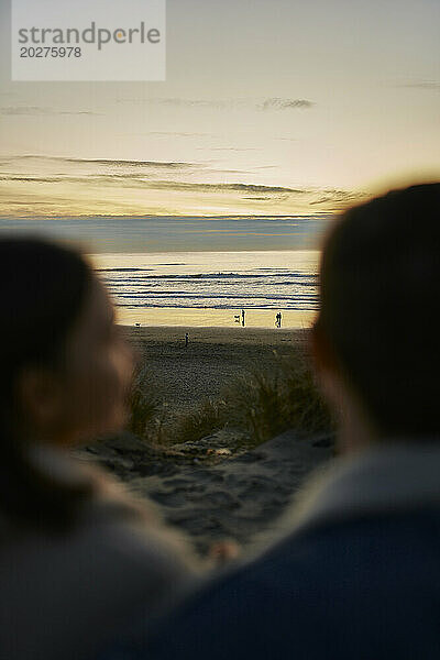 Junges Paar blickt am Strand auf das wellige Meer
