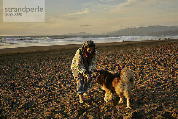 Glückliche Frau  die am Strand mit Hund spielt