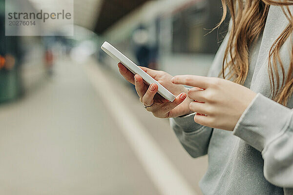 Frau surft mit Smartphone am Bahnhof im Internet