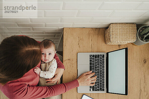 Freiberufliche Mutter tippt auf Laptop und hält Baby