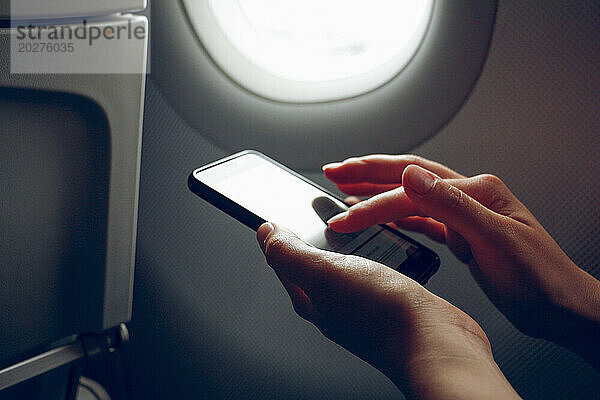 Hände einer Frau  die im Flugzeug über ihr Smartphone im Internet surft