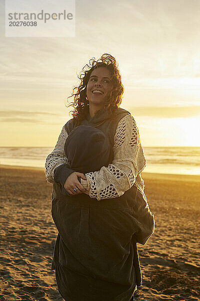 Junger Mann trägt lächelnde Frau am Strand