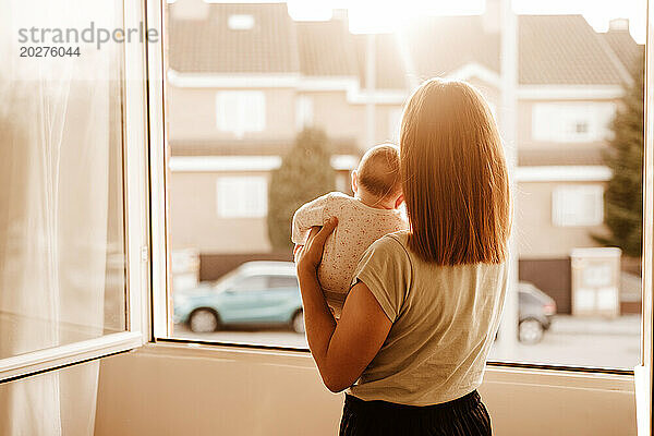 Mutter trägt ihre kleine Tochter und schaut durch das Fenster