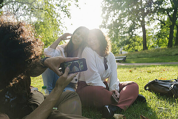 Junger Mann fotografiert Freunde per Smartphone im Park